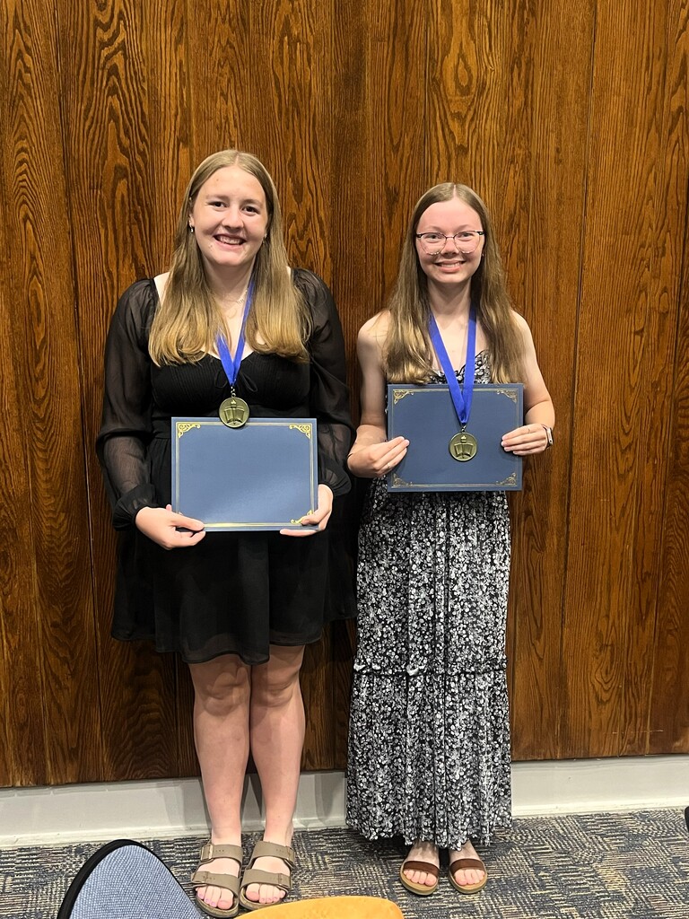 Group photo of two students wearing medals and carrying blue folders