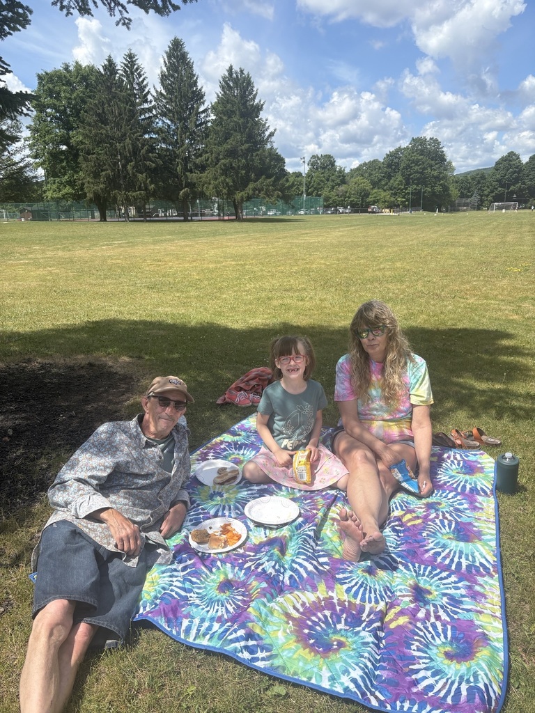Two adults and child sitting on blanket for a picnic