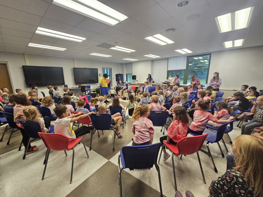 Students gathered in classroom looking at adult in yellow shirt