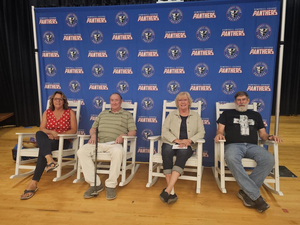 4 retirees sitting in rocking chairs in front of panther banner