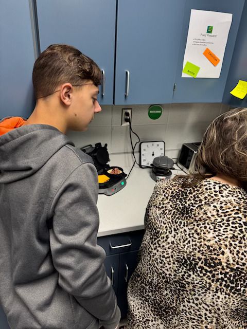 Picture of a student watching a teacher prepare food in the Cougar Cafe.