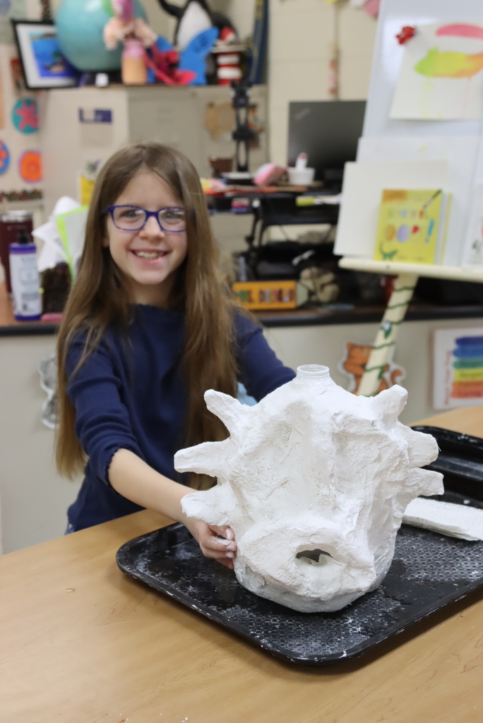 Student smiling while working on paper mache head on milk jug