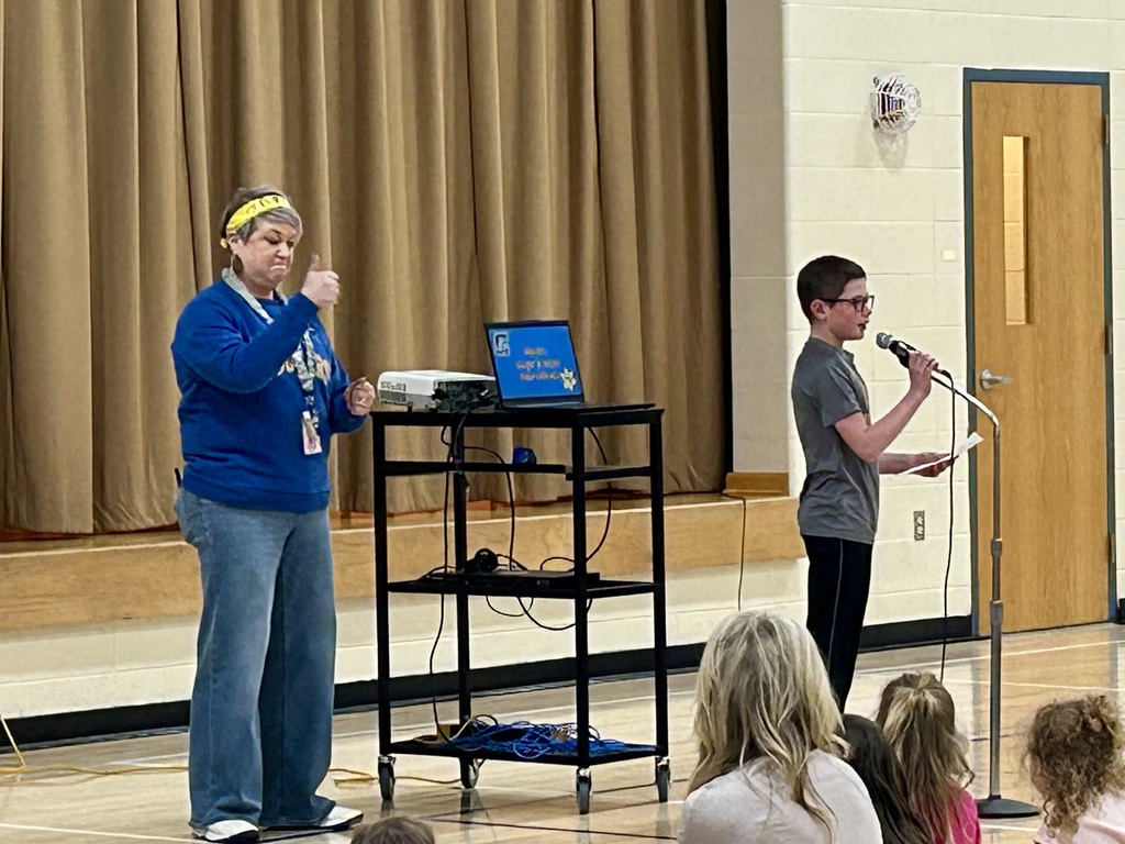 Ms. Boycks giving a thumbs up well a student council member speaks into the microphone