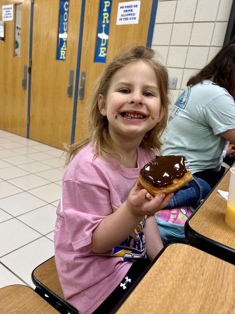 Student in pink shirt, eating a donut, chocolate on her face