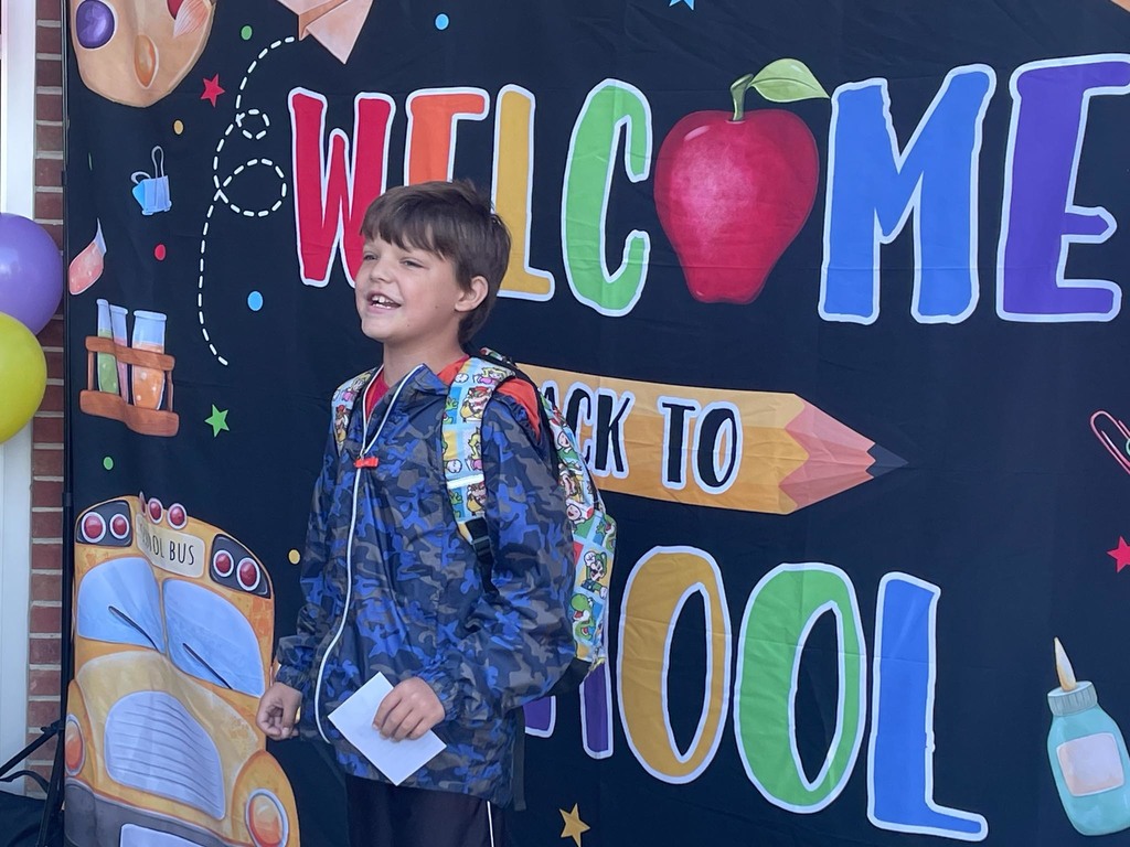 A student stands in front of a sign reading Welcome Back to School