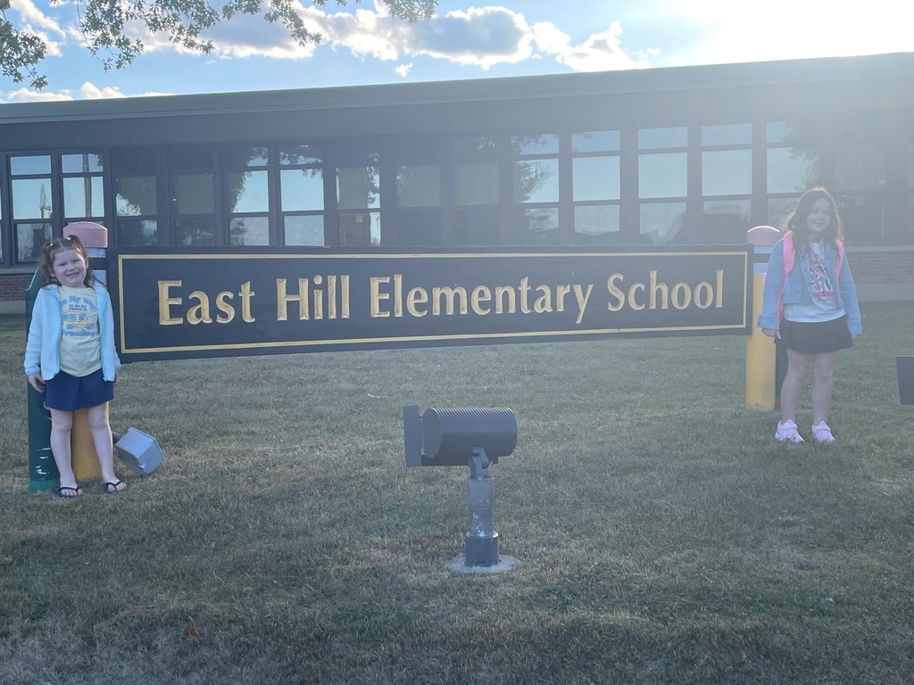 Two children stand in front of a sign reading "East Hill Elementary School"