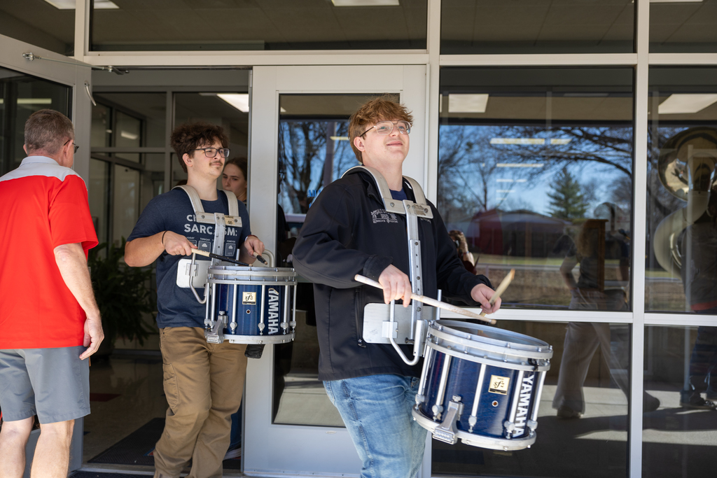 Student smiling carrying a snare drum during a pep rally in front of the school