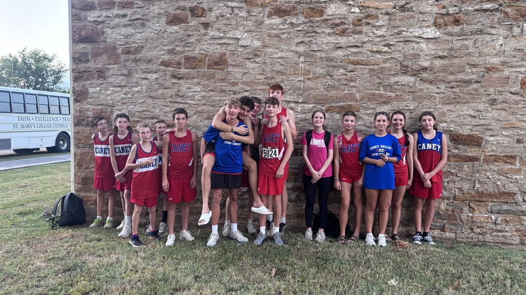 Candid group photo f cross country team after an event standing in front of stone wall.