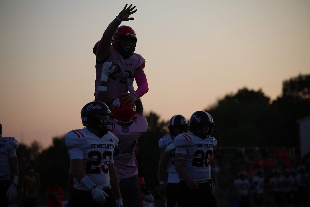 A Caney Valley football player raises his hand while being lifted by a teammate during a game against Humboldt at sunset.