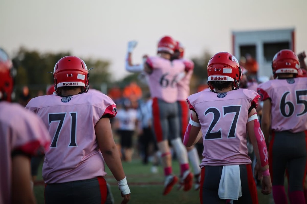 Caney Valley football players wearing pink jerseys and red helmets walk onto the field during a Pink Out game.