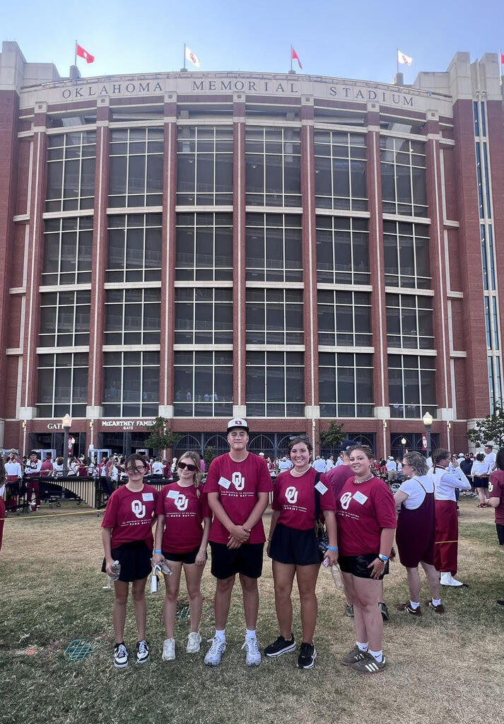 Students stand in front of the stadium at OU in matching OU band tee shirts