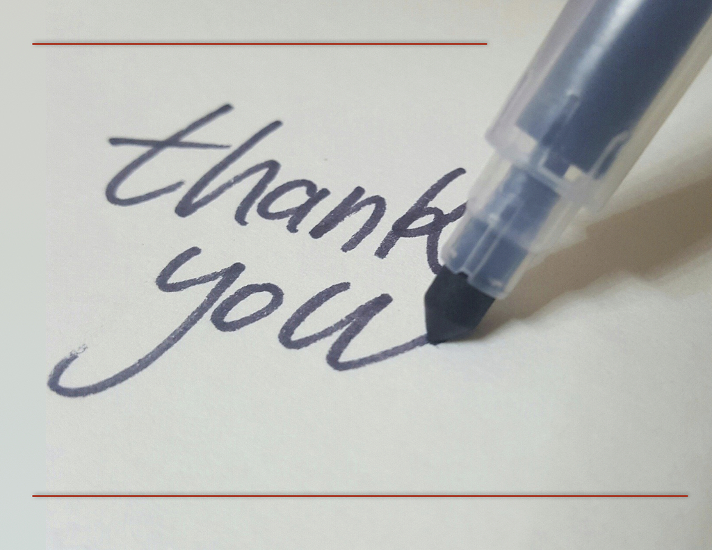 image of pen writing the words "Thank you" on a piece of paper.