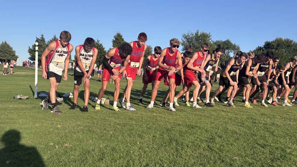 Caney boys cross country runners in red uniforms lean forward at the starting line alongside runners from other schools.