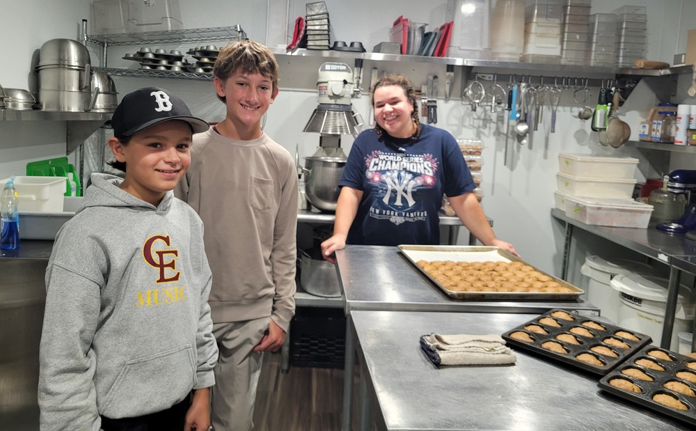 two male students at a bakery with a female baker