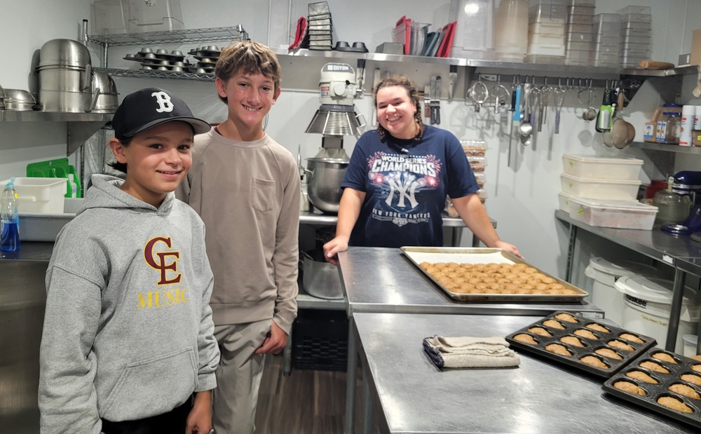 two male students at a bakery with a female baker