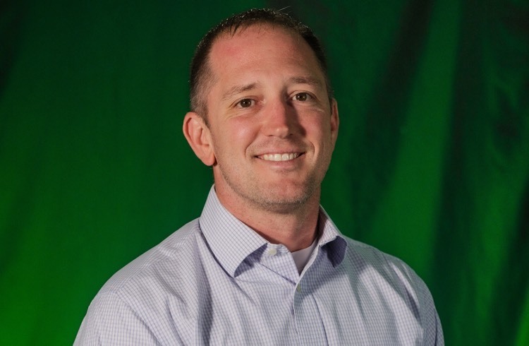 a man smiles at the camera in front of a green backdrop 
