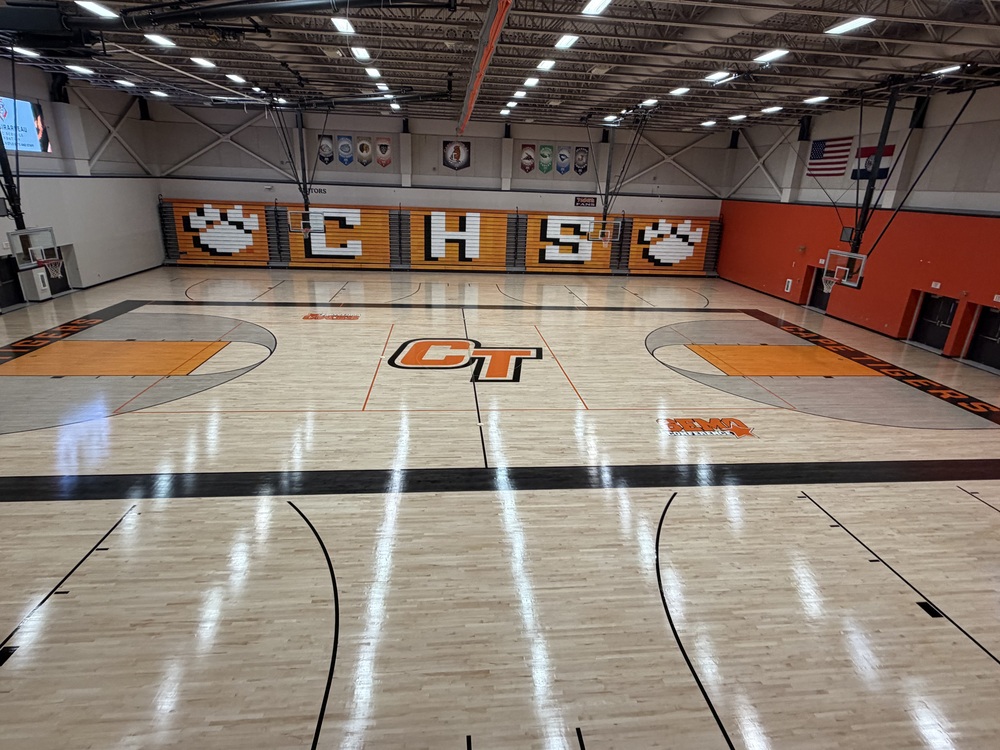 A light wood basketball court with a CT logo in the middle