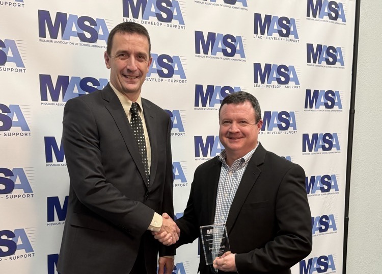 two men pose for the camera - one with an award