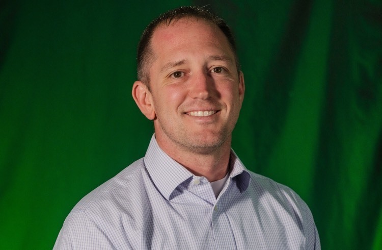 a man smiles at the camera in front of a green backdrop 