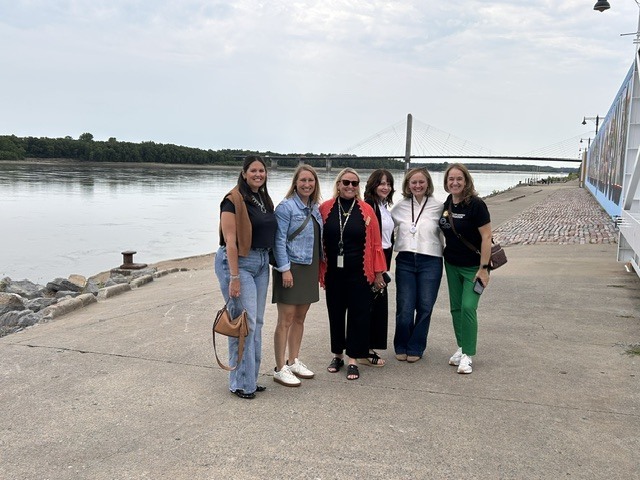 Better Together, Six women representing school foundations pose together along the Mississippi River in downtown Cape Girardeau. The Bill Emerson Memorial Bridge is visible in the background. The group gathered to connect, share ideas, and learn from one another while visiting Cape Girardeau. 
