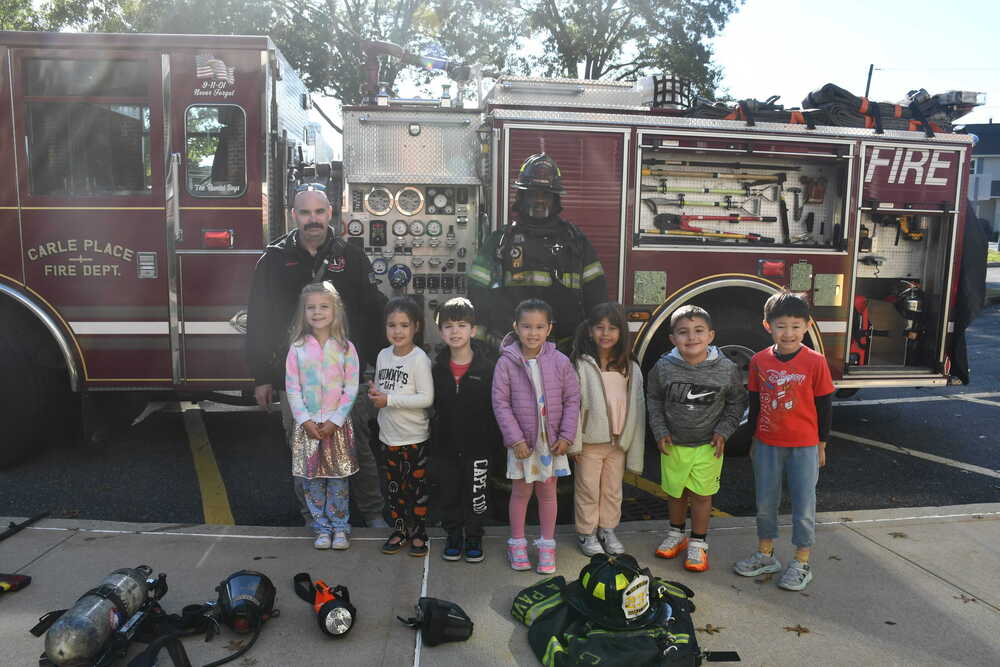 Firefighters smiling with children outside of fire truck.