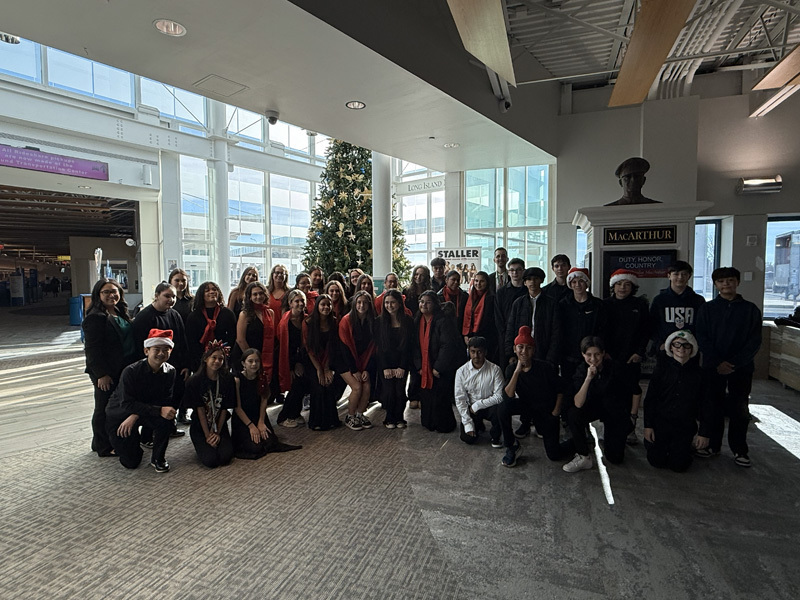 A group of people in festive attire pose indoors near a tall, decorated Christmas tree