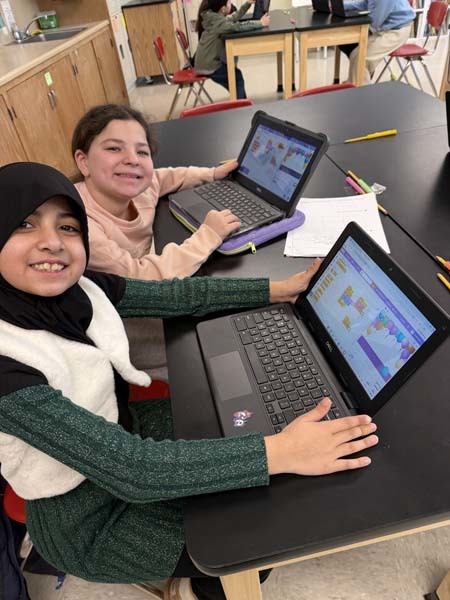 Students smiling, working on laptops.
