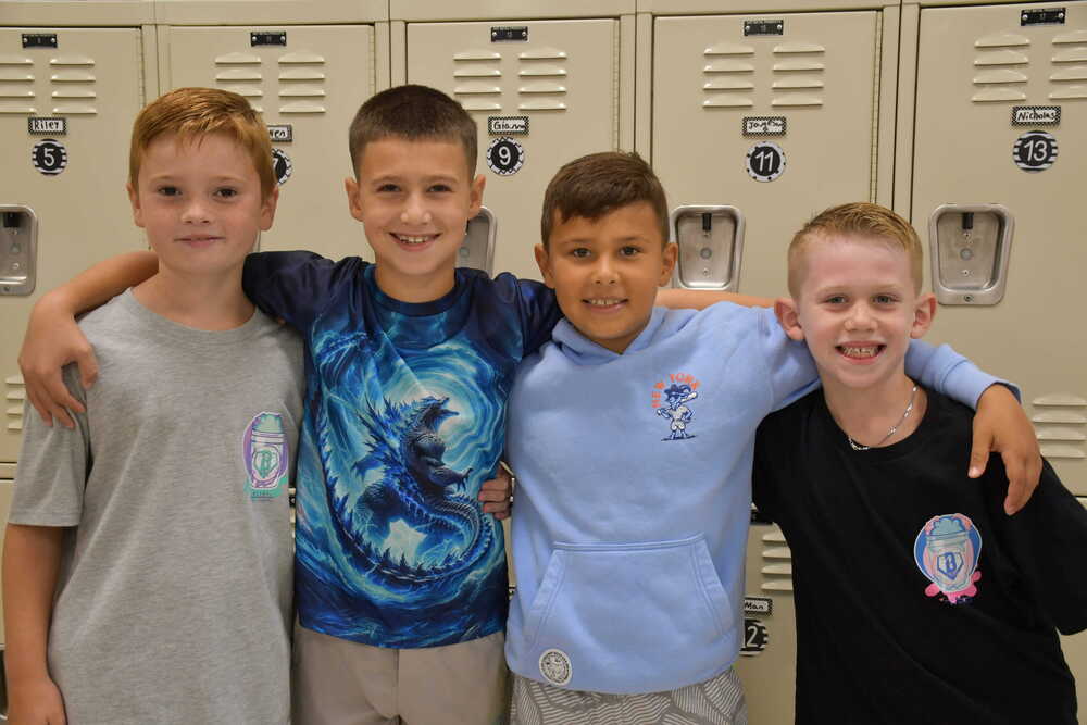 Four boys smiling in front of lockers.