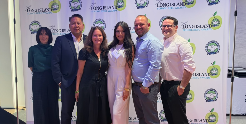 A group poses in front of a banner for the Long Island School Hero Awards.