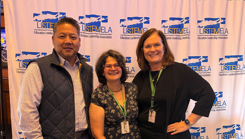 Three adults standin in front of LSITEMELA banner