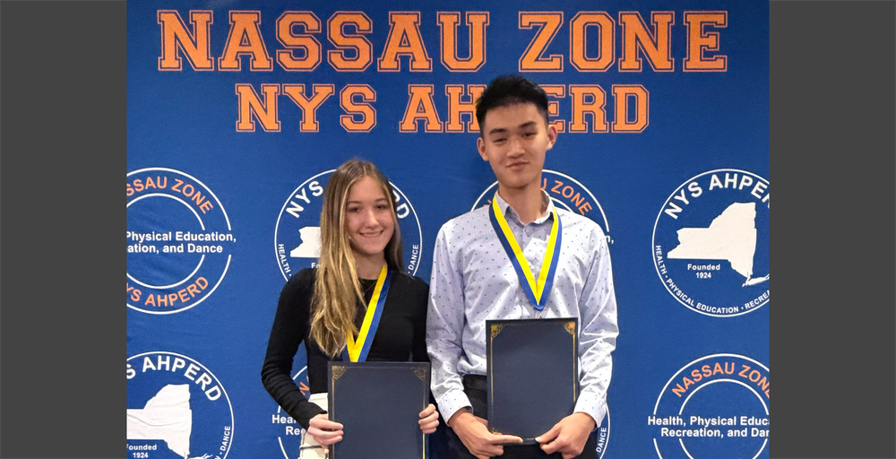 Two students stand proudly with certificates and medals in front of a blue "Nassau Zone NYS AHPERD" banner