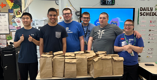 Students standing togehter in front of brown paper bags.
