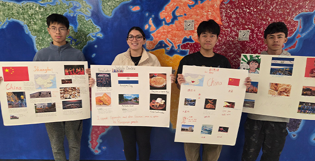 Students holding their projects in front of map of world.