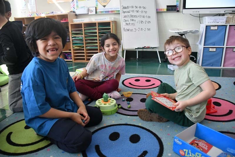 Students sitting, smiling on carpet.