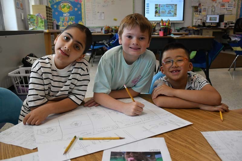 Three students smiling at the camera while working on projects.