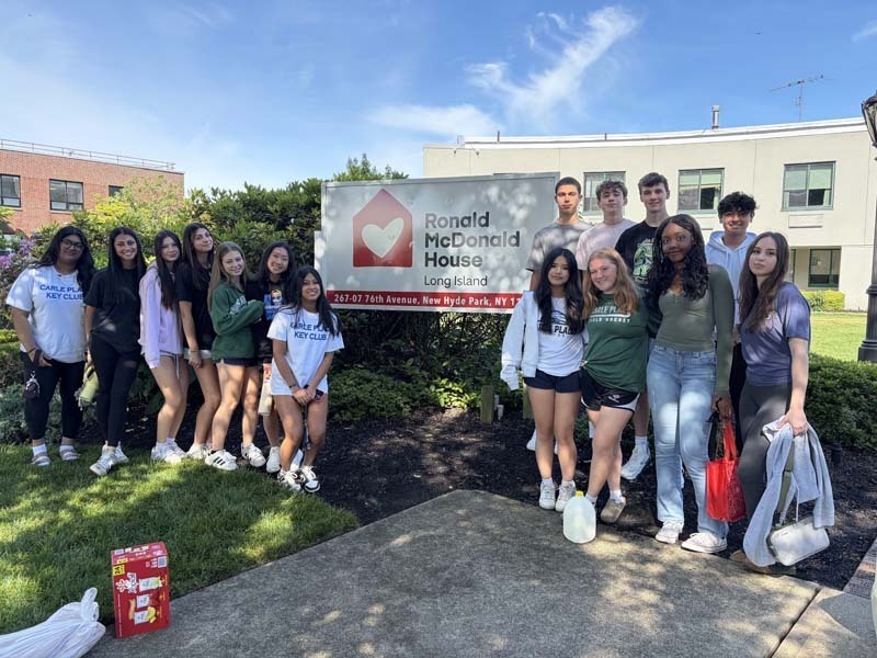 Group of students smiling outside by banner.
