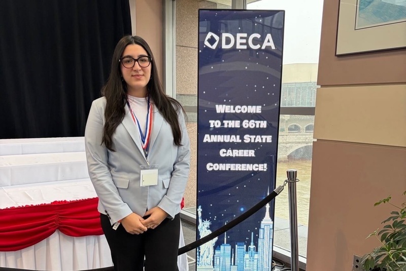 Student posing near DECA billbooard.