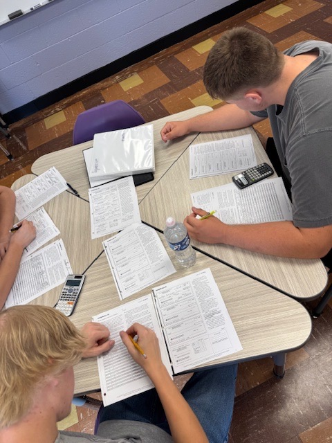 3 students sit at a desk and work on balance sheets