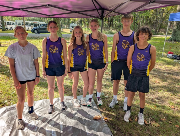 6 members of the cross country team stand under a tent outside in their uniforms