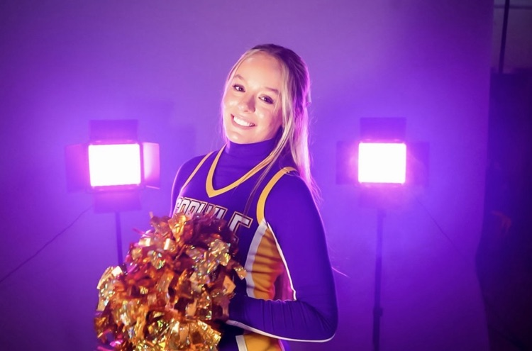 female cheerleader smiling in purple smoke with 2 lights behind her