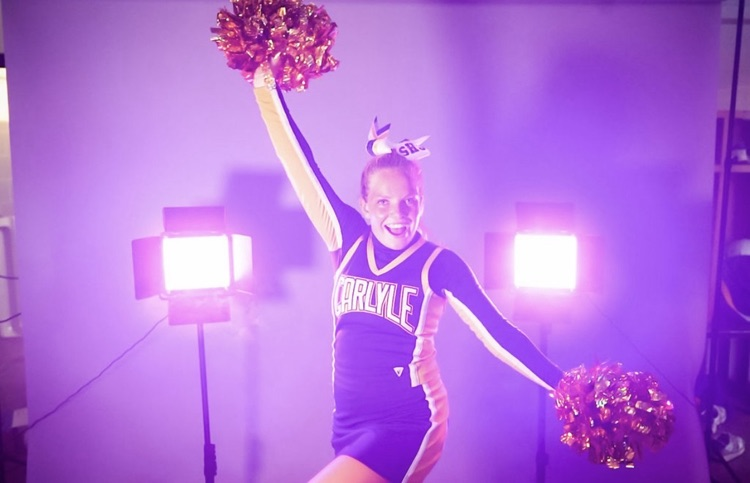 female cheerleader with pom poms in a room filled with purple smoke and 2 back lights