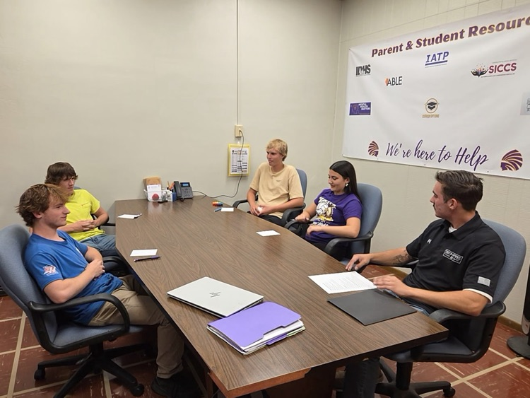 Tanner sits at a large table talking to group