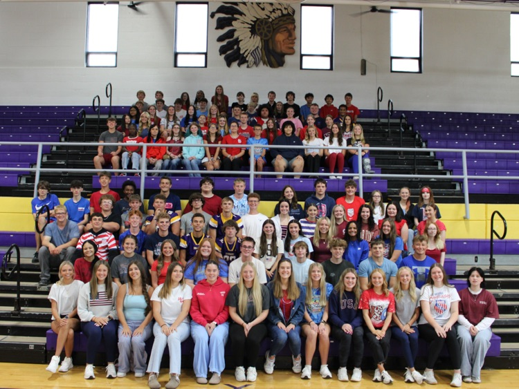 Group photo of all students in the gymnasium, wearing red white and blue