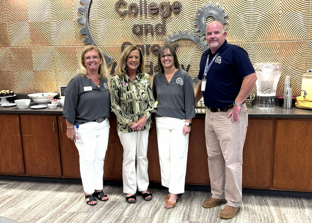 four people pose in front of a sign in the lobby of a school