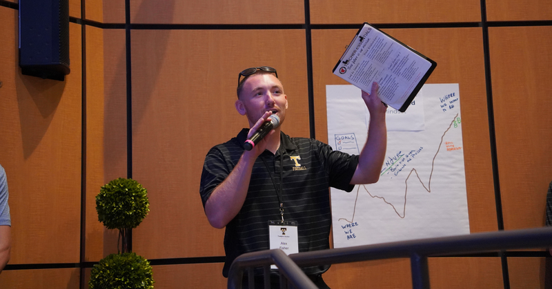 a new teachers holds up a clipboard while speaking into a microphone