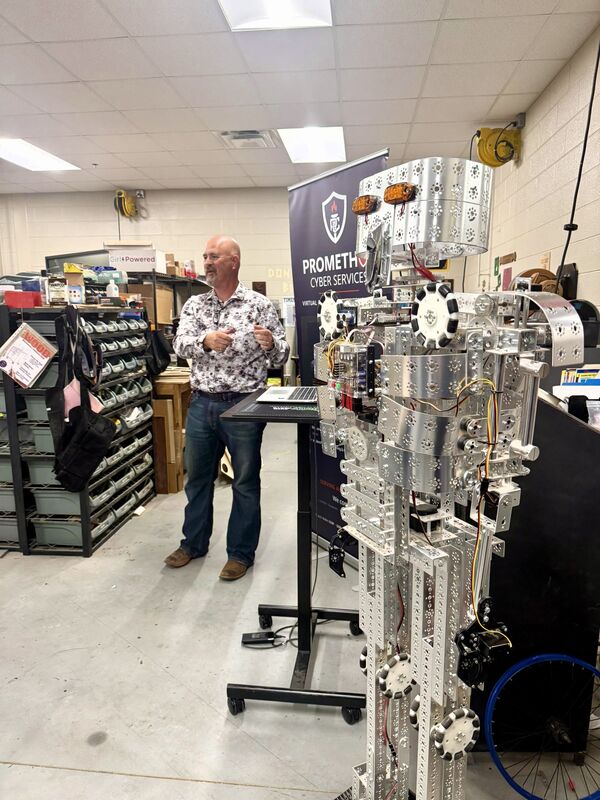 a man addresses a crowd from behind a silver robot