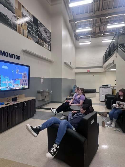 Three students sit on couches and play a Mario game on a Nintendo Switch.