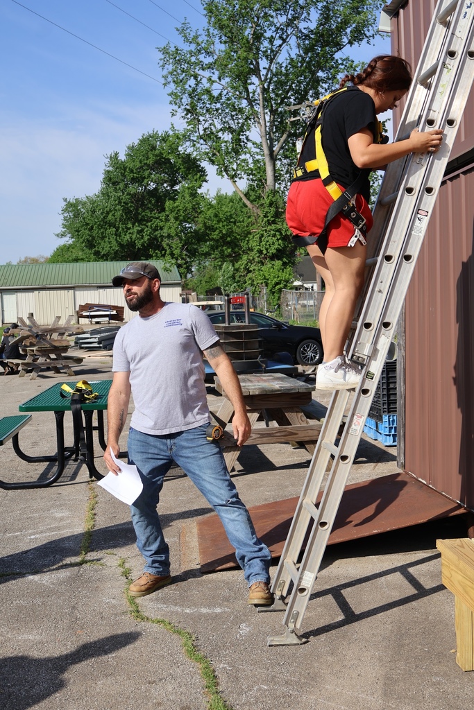 Student climbing down ladder while teacher braces ladder