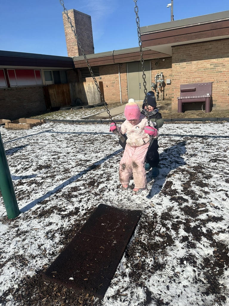 Child swinging on swing while another child is helping them.