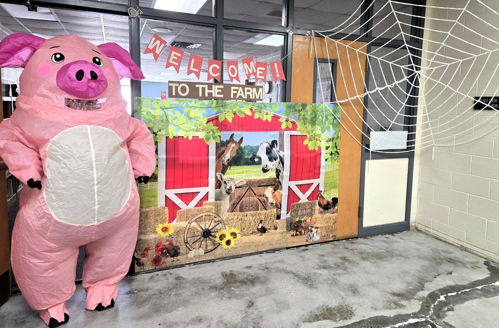 Mrs. Good dressed in an inflatable pig costume posing by a barn poster and a giant spider web.